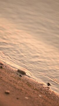 Quiet waves and coastal sand, close-up, evening time, orange light.
