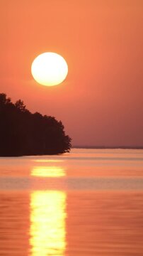 sun setting behind the sea horizon, a tropical island and quiet waves in the foreground, orange light, glare on the water.