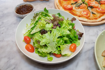 Fresh salad with vibrant tomatoes on the plate and pizza background
