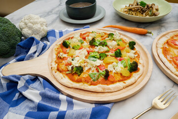 Vegetable pizza served on a wooden board with various vegetables and pasta