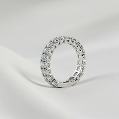 Close up view of a silver eternity ring with diamonds on a white surface in soft lighting