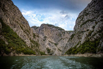 Steep limestone cliffs and narrow water passage at Lake Koman in northern Albania, surrounded by rugged mountain scenery and calm green water.