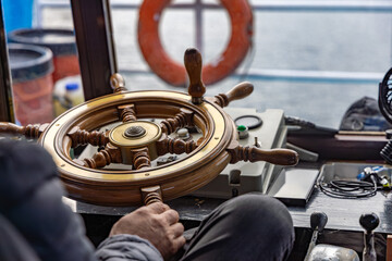 Wooden ship wheel and navigation controls inside a ferry wheelhouse, with a view of water and mountains through the windows. © Christo
