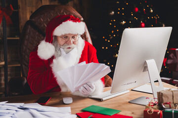 Santa Claus sits at a desk in a warm home office sorting papers beside a Christmas tree with lights and gifts creating a festive busy day vibe