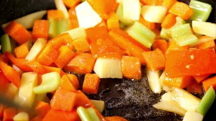Diced vegetables are sautéed in a hot pan in this close up. A spatula stirs a colorful mix of carrots, celery, and peppers sizzling in oil. - Powered by Adobe