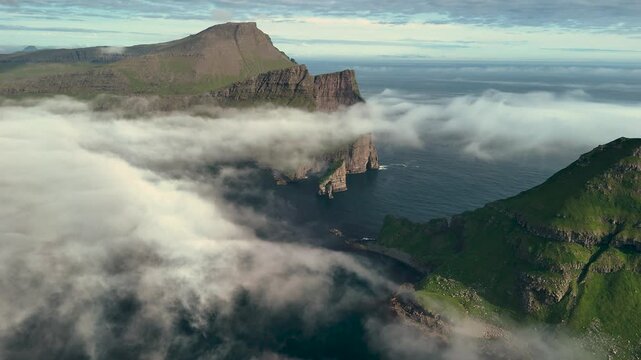 Experience breathtaking views of the towering cliffs and dramatic landscape at Drangarnir in the Faroe Islands. The ethereal mist blankets the ocean, creating a magical atmosphere at sunrise.