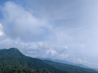 Aerial view of green mountain landscape with clouds and blue sky.
