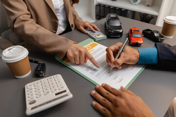A business meeting between a car dealer and a client discussing vehicle purchase agreement. The contract is being reviewed and explained before signing, representing trust and cooperation.