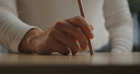 A detailed view of a hand poised with a pencil, ready to write or draw on a smooth wooden surface.