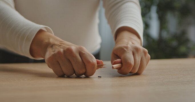 Close up of woman hands breaking a pencil on a wooden table, symbolizing stress or frustration.