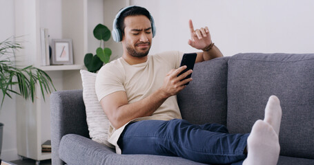 Obraz premium Happy, phone and music with man on sofa for streaming, radio station and audio playlist. Podcast subscription, headphones and media platform with person in living room of home for connection