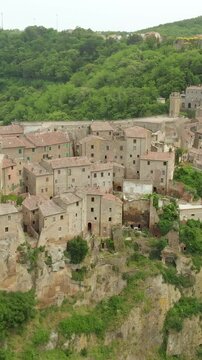 Aerial summer afternoon view of Sorano. Rooftops of an ancient medieval hill town hanging from a tuff stone over the Lente River. Etruscan heritage. Province Grosseto, Tuscany, Italy. Vertical footage
