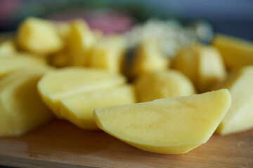 Raw potato slices, close-up, shallow depth of field. Potatoes cut into wedges on a cutting board.