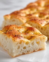 Close-up of a Slice of Freshly Baked Focaccia Bread with Herbs and Salt on a White Surface, Eye-Level Shot
