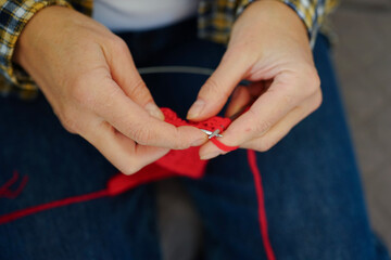 Woman in checkered shirt knitting red fabric with needles, top view. Cozy and creative atmosphere.