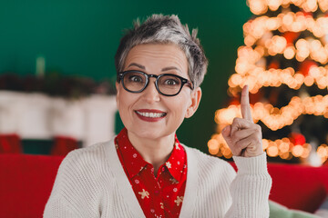 Charming senior woman in festive attire celebrating Christmas indoors with bright holiday lights...