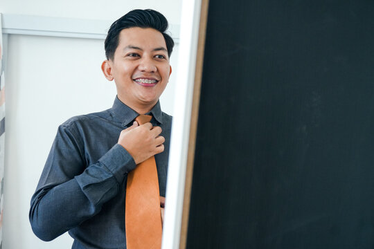Confident Young Businessman Adjusts His Orange Tie Smiling In Preparation For Success