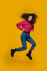A Joyful and Cheerful Young Woman Enthusiastically Jumping Against a Bright Yellow Background