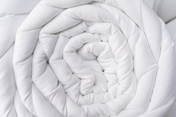 Rolled white quilted blanket or comforter tied with a blank kraft paper band, isolated on a white background. Texture of quilted fabric.Perfect for textile and bedding mockups, packaging, store design