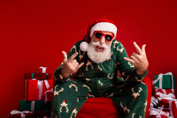 Santa in green Christmas pajama sits with gifts on red background for festive stock photography