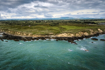 Aerial view of rugged Irish coastline with rocky cliffs, green headland, and turbulent turquoise...