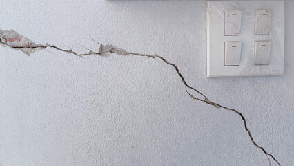 white concrete wall has cracks due to poor quality construction. Cracked wall surface, earthquake cracked.