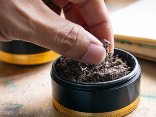 Person Finger Testing Texture of Crushed Dry Marijuana in Premium Herb Grinder