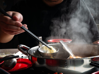 Person eating hot pot shabu shabu with chopsticks and steaming broth in divided metal pot at restaurant table