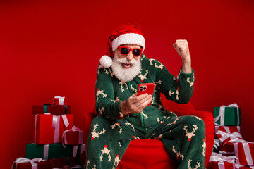 Santa in green reindeer pajama with phone among gifts creates Christmas fun and cozy festive vibes
