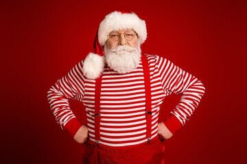 Santa in striped shirt with red suspenders posing in bright red studio for Christmas promotion and...