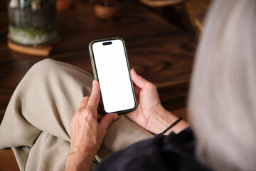 Elderly woman holding smartphone with blank white screen sitting on comfortable sofa at home