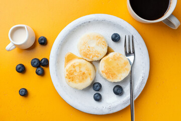 Syrniki, cottage cheese fritters served with blueberries, cream on a plate. Top view. Healthy breakfast meal