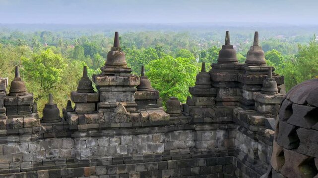 Explore ancient stone structures at Borobudur Temple surrounded by lush green jungle in Central Java, Indonesia during clear sunny weather. Gimbal shot