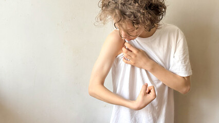 Curly Teen Boy Flexing Arm And Looking At Muscle Indoors In Daylight For Concepts Of Body Image, Self-Awareness, Teenage Identity, Confidence Development, And Relatable Visuals For Youth Mental Health