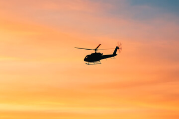 Helicopter silhouette at dusk gliding smoothly. Golden sky paints a stunning backdrop. Air transportation at sunset, captured in a serene flight scene.