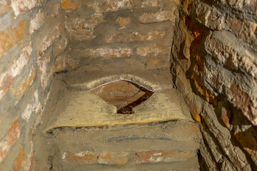 Ancient narrow toilet hole in the thick stone walls of Prejmer fortified church, Transylvania, medieval defensive architecture and dark interior texture. UNESCO site of Romania
