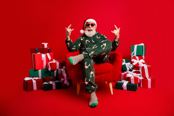 Santa in cozy sleepwear sits in a red armchair surrounded by gifts smiling a festive scene perfect...