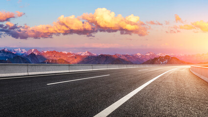 Empty asphalt highway leading towards a majestic mountain range at sunset © ABCDstock