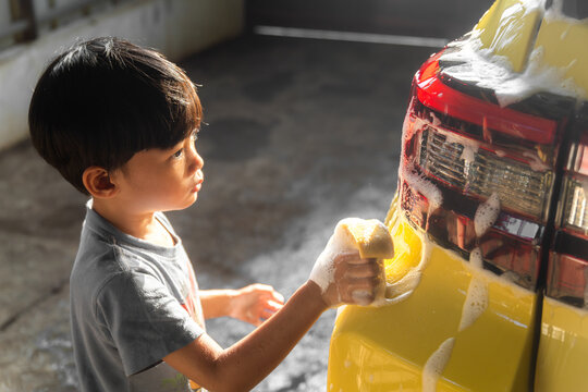 Little boy washing a yellow car with sponge and soap foam under sunlight