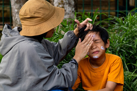 A mother applying sunscreen lotion to her sons face before outdoor activities