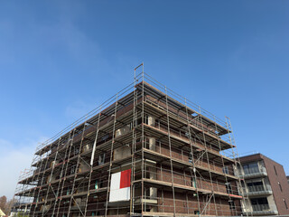 Construction site featuring a multi-story building under scaffolding, showcasing brickwork and a clear blue sky, illustrating the progress of urban development and architectural design