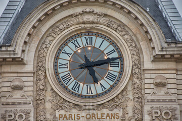 Clock at the former Musee d'Orsay train station in Paris with classical architecture and a cloudy sky in the background