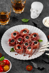 Halloween snacks. Eyeballs cooked from jamon, mozzarella cheese and olives on a plate on a dark background. Top view.