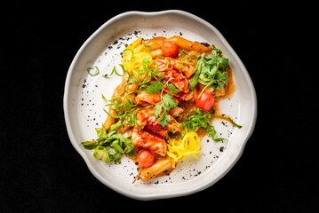 Gourmet dish with glazed meat, yellow squash, cherry tomatoes, and fresh herbs in a white bowl. Dark, moody background with selective focus.