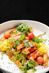 Gourmet dish with glazed meat, yellow squash, cherry tomatoes, and fresh herbs in a white bowl. Dark, moody background with selective focus.