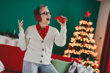 Elderly Woman Enjoying Music and Festive Holiday Atmosphere at Home Near a Decorated Christmas Tree