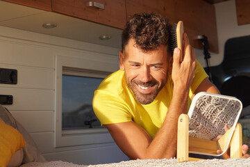 Nomadic and van life style. Man in a yellow T-shirt combing his hair in front of a mirror