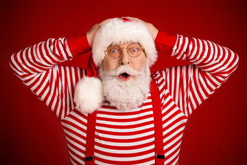 Cheerful Santa Claus in striped costume with surprised expression posing against red background for...