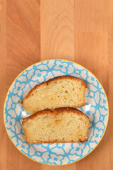 A vertical overhead shot featuring two slices of moist yellow cake with a golden crust, presented on a decorative blue and white plate on a light wooden surface