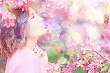 Fototapeta premium Springtime background, a woman in pink in a blooming cherry orchard, a model posing in a romantic style